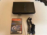 Top view of PS2 console, Gran Turismo 3 game case, AV cable, power cord partially coiled
