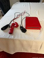 Red Wii console, red Wii Remote, two black Nunchuks on bed