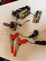 Lot overview showing two NES controllers, two Zapper light guns, Recoton joystick with cords