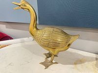 Side view of bronze goose figurine showing gold tone finish, feather detail, webbed feet