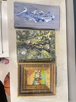 Three paintings laid out: framed village scene, blue botanical, green foliage