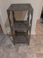 Full view of metal stand showing three shelves and decorative sides