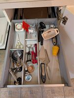 Top drawer view showing measuring cups, spoons, shears, scoop, server, zester and other utensils