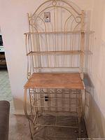 Full view of beige metal baker's rack showing shelves, wood top, wine rack
