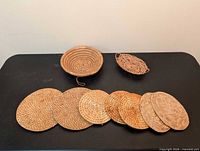Overhead view of seven woven trivets and two small baskets on black surface