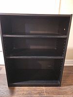 Front view of black bookshelf showing three adjustable shelves and peg holes