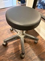Full view of black faux leather swivel stool with five-star plastic base and casters