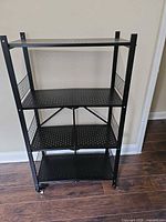 Front view of black metal folding shelving unit with four shelves