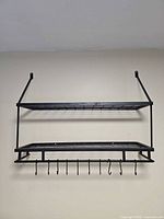 Full front view of the black metal pot rack showing two shelves, hanging bar and hooks