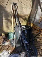 Wheelbarrow on side with attached wheel, two wood-handle shovels and green snow shovel visible