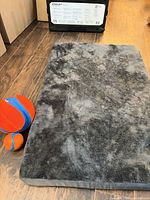 Gray faux-fur rectangular pet bed with two Chuckit balls for scale