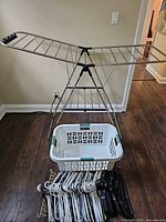 Foldable metal drying rack set up, laundry basket below, pile of hangers