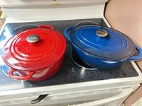 Red and blue Dutch ovens with lids on stovetop