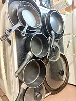 Overall lot on stovetop including cast iron skillets, nonstick pans, glass lids, perforated pizza pan