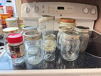Group of assorted mason jars, flip-top jar, swing-top bottle, Amarula tin and coffee jar on stovetop