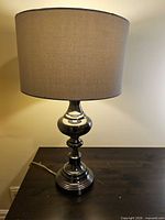 Full view of lamp on table showing chrome base and gray shade