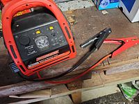 Front view of MotoMaster booster showing control panel, LED light, ports and attached jumper cables