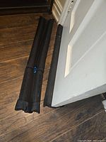 Two black door draft stoppers placed alongside open door on wood floor