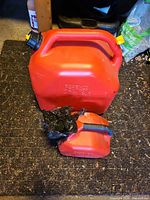 Large 25 L and small ≈5 L Scepter red fuel cans on floor mat