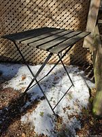 Full view of square wood-slat bistro table on folding metal legs outdoors