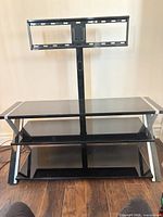 Full view of TV stand showing three glass shelves, metal frame, fixed mount