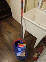 Full mop and bucket with boxed refill beside utility sink