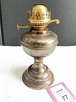 Front view of metal oil lamp showing pedestal base, reservoir and brass burner