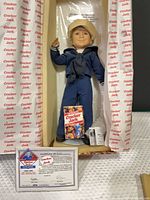 Doll in open Cracker Jack box with accessories and COA visible
