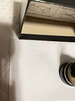 Embosser with impression on paper, box partially visible