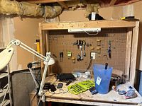 Pegboard workbench with hand tools, Ryobi bit set, blue tote, caster wheels partially visible