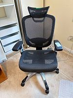 Full view of black mesh ergonomic chair showing headrest, armrests, seat, and base