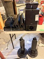 Full lot showing amplifier, subwoofer, two rear satellites on sub, floor satellites on stands