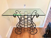 Front view of metal wine rack console table showing glass top and bottle holders