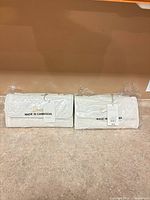pair of new white woven clutches in plastic with tags visible