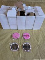 Four closed boxes with compact mirrors, two sample units showing graphics, two units showing mirror side