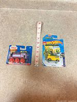 Both packaged toy vehicles with tape measure for scale