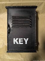 Front view of black metal key cabinet showing stencil text and louvers