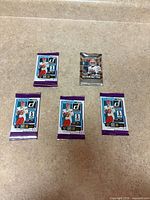 Five unopened football trading card packs; four Donruss 2025 and one Prizm Draft Picks 2023