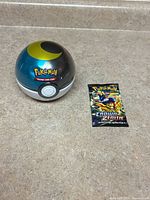 Poké Ball tin and sealed booster pack side by side