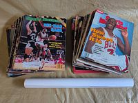 Two stacks of Sports Illustrated magazines and one rolled white tube containing poster