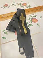 Full view of black guitar strap with gold cross and adjustment slots