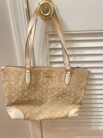 Front view of Coach beige jacquard shoulder bag hanging on door