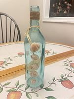 Full view of aqua glass bottle front showing shells and twine neck wrap