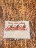 Front view of closed display holder showing graphic and three coin recesses