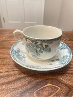 Front view of tea cup on matching saucer displaying floral transfer pattern