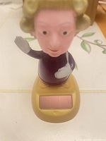 Front view of Queen Elizabeth II solar figurine showing waving pose and solar panel on base