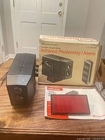 front view of alarm unit beside box, reflector lens and manual visible