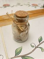 Front view of small glass bottle filled with shells, cork stopper and raffia tie visible