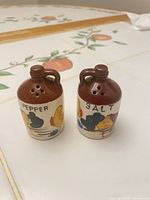 Front view of both shakers showing brown tops, handles, hand-painted decoration and labels