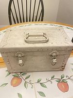 Front view of white metal trunk showing handle, twin latches, riveted edges